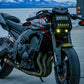 A sleek black Yamaha FZ motorcycle with custom vertical LED headlights, red accents, and 'SUPERBIKES' branding on the engine cover, parked in front of a blue sky and white wall backdrop